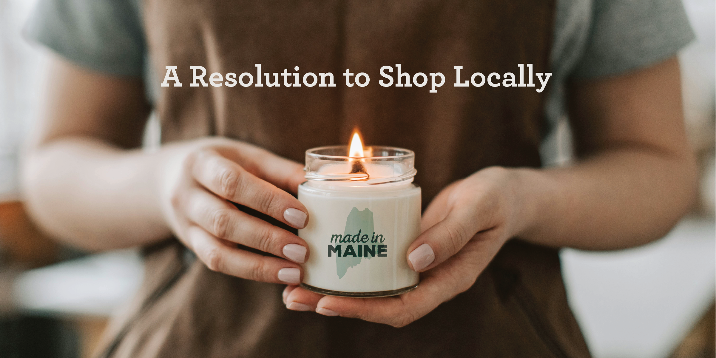 A person holding a lit white candle in a jar that says Made in Maine.